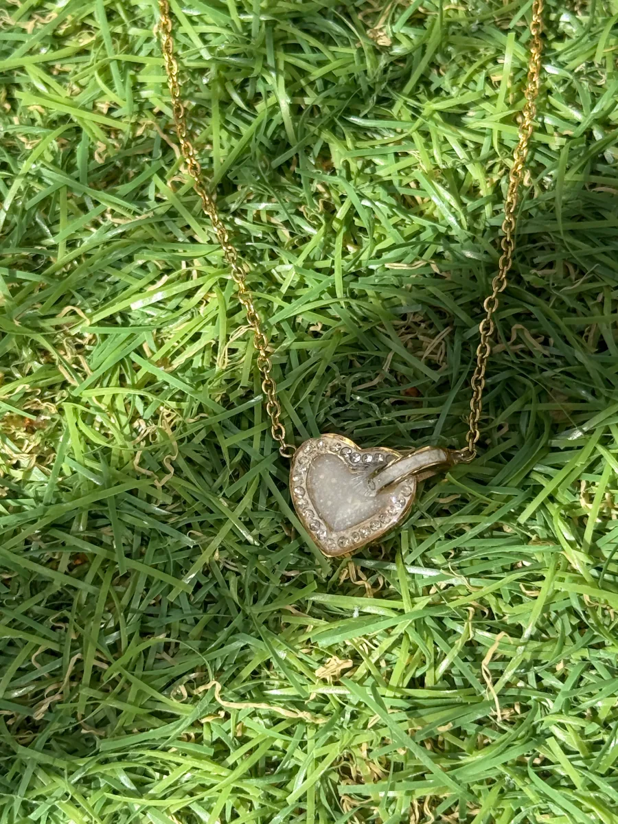 Pendentif cœur au lait maternel sur chaîne dorée, posé sur l'herbe