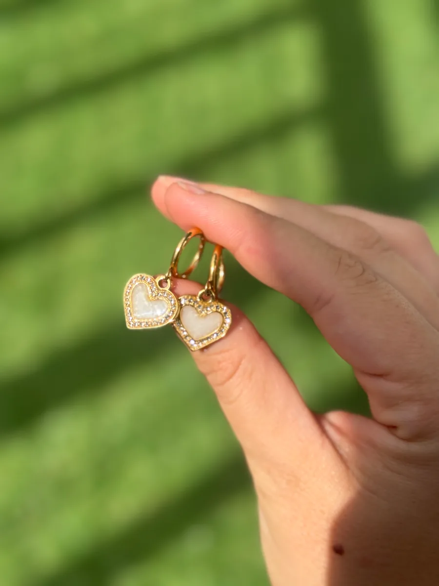 Boucle d'oreille cœur au lait maternel tenue entre les doigts, au soleil