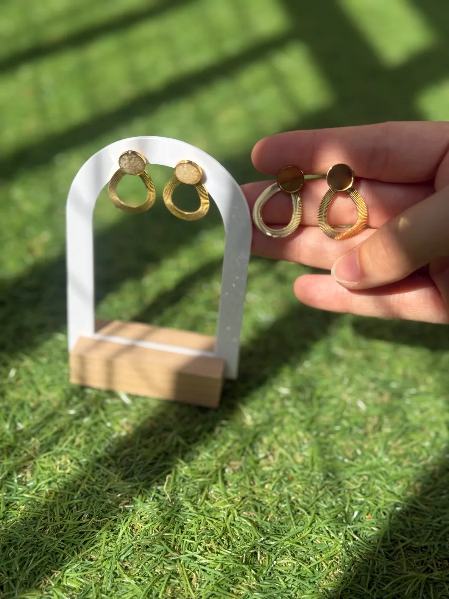 Boucles d'oreilles gouttes au lait maternel tenues à côté de leur présentoir