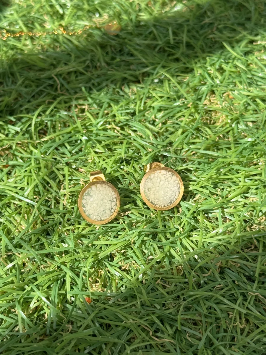 Deux puces rondes au lait maternel en acier doré, posées sur l'herbe