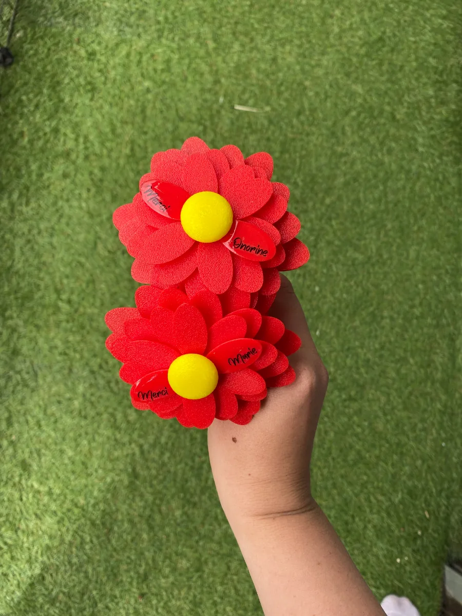 Deux fleurs rouges en feutrine et cœur jaune tenues sur fond de gazon