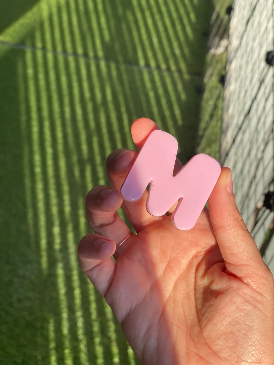 Lettre M en résine rose, face colorée de l'initiale au cordon ombilical