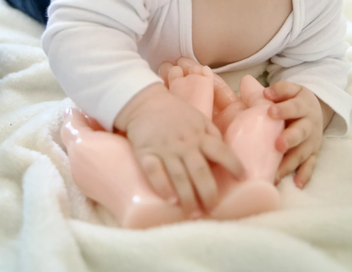 Petites mains de bébé sur la sculpture en résine de ses pieds, posée sur une couverture blanche