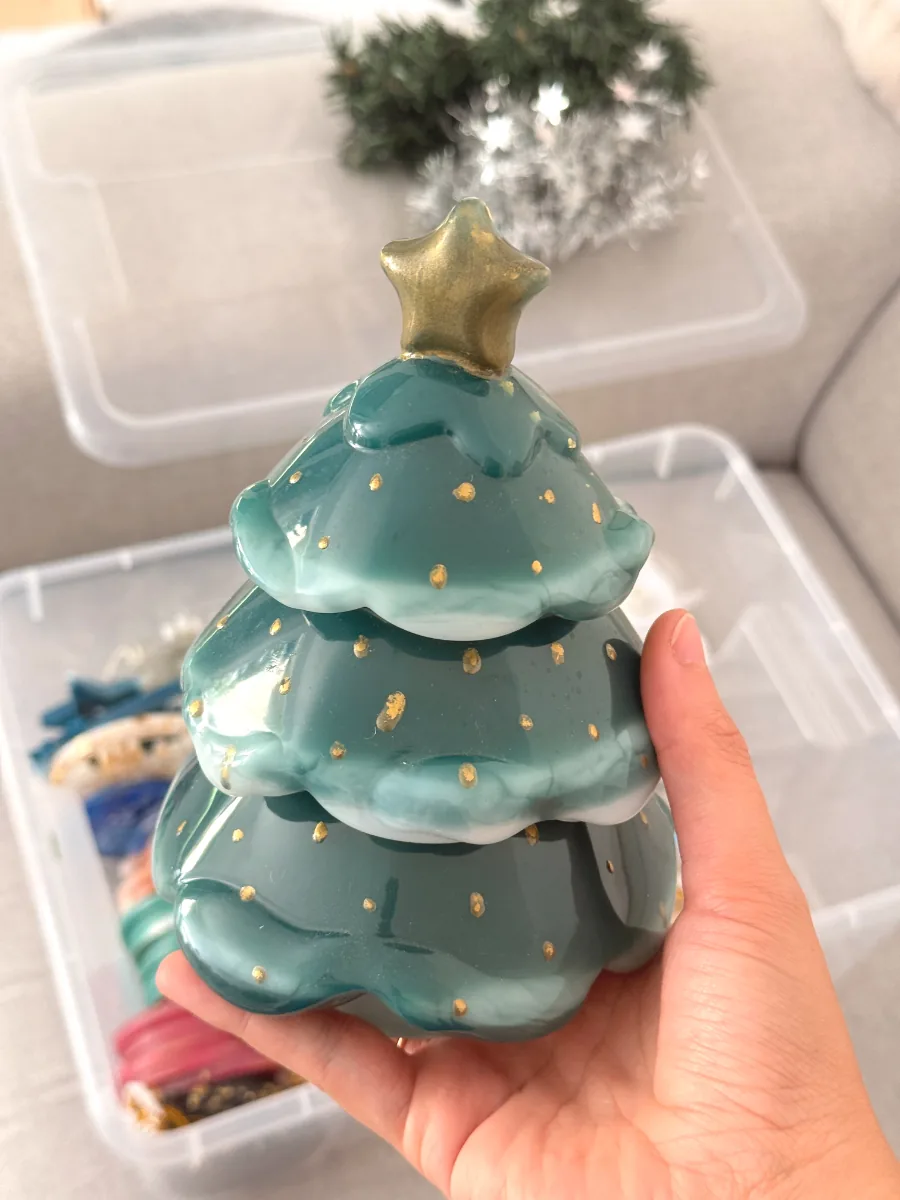 Sapin de Noël vert à étoile dorée qui cache une boîte à bijoux, tenu en main