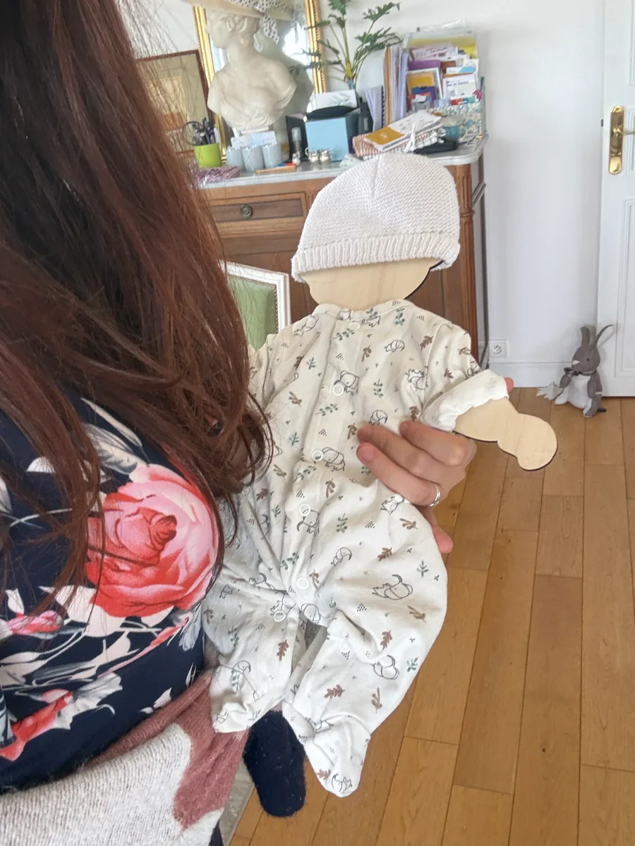 Maman tenant la silhouette en bois habillée des vêtements de naissance de son bébé