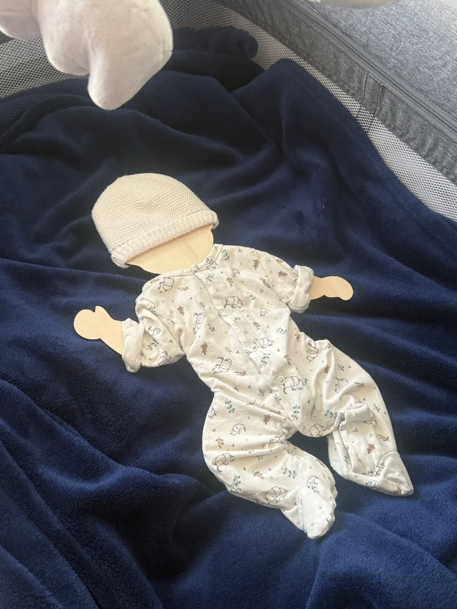 Silhouette de bébé en bois habillée d'un pyjama fleuri, sur une couverture bleu marine
