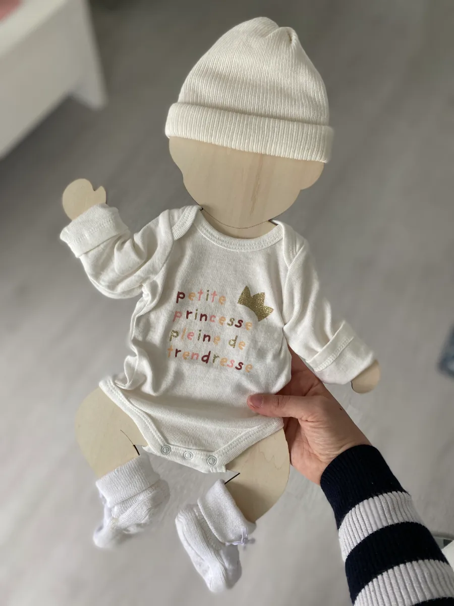 Silhouette de bébé en bois portant body, bonnet et chaussettes de naissance