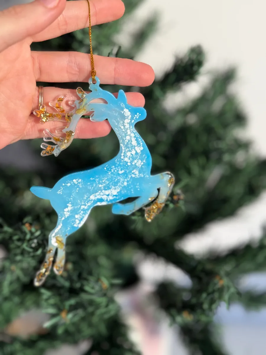 Cerf de Noël bleu ciel et or tenu devant un sapin