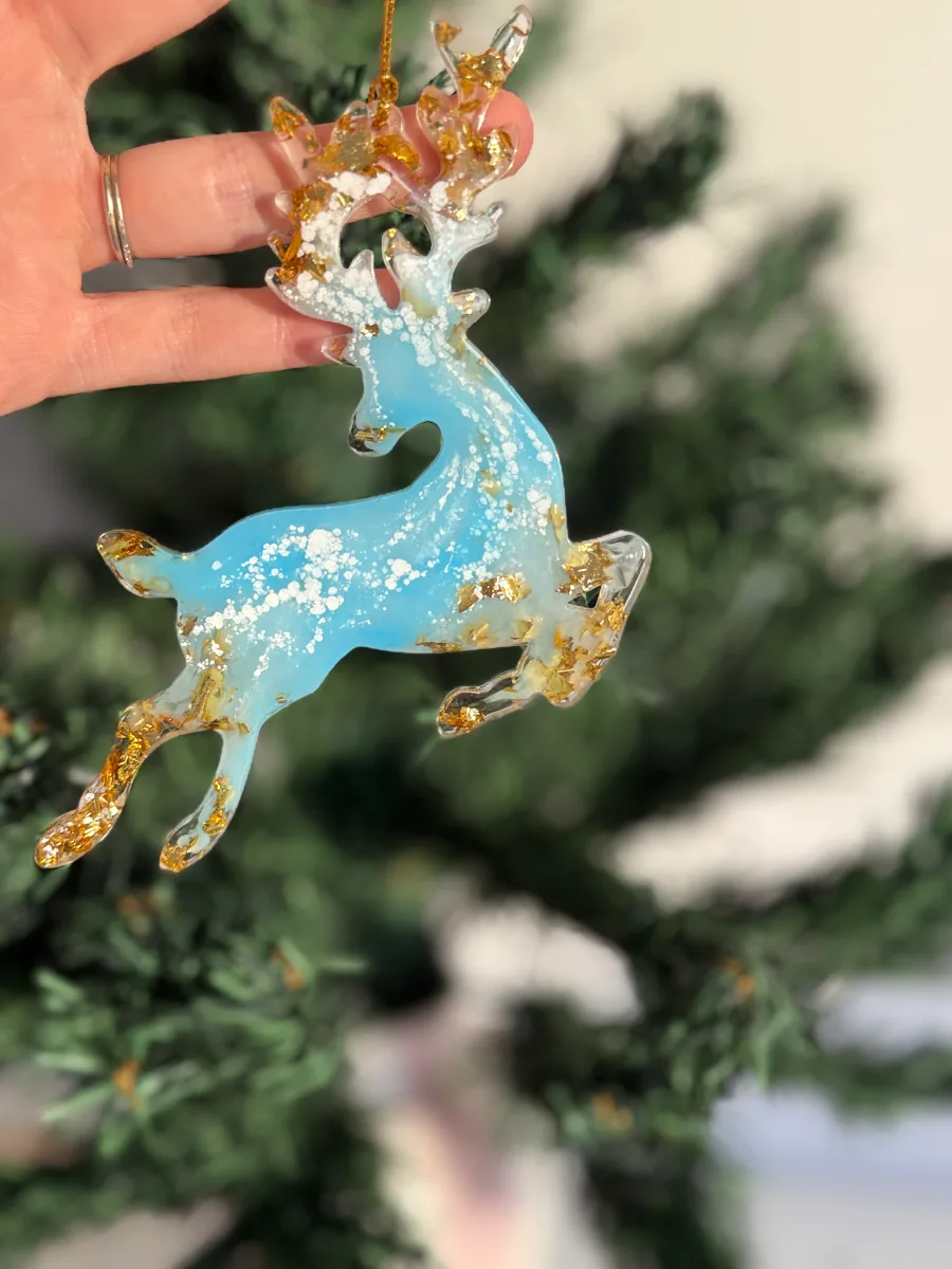 Cerf de Noël bleu et or bondissant, tenu devant le sapin
