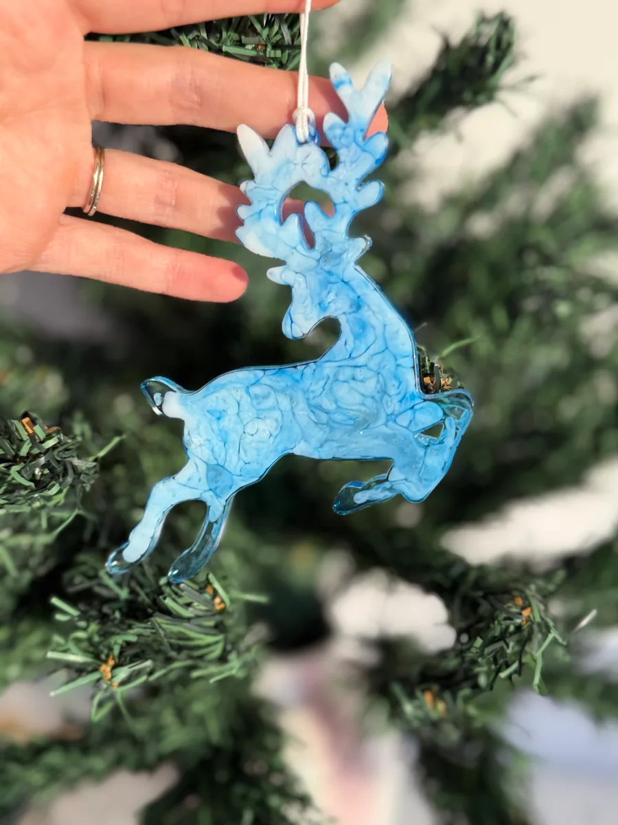 Cerf de Noël bleu marbré en résine devant un sapin