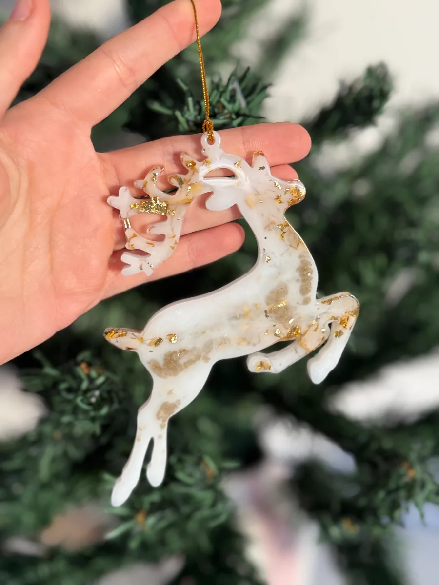 Cerf de Noël en résine blanche et dorée devant un sapin