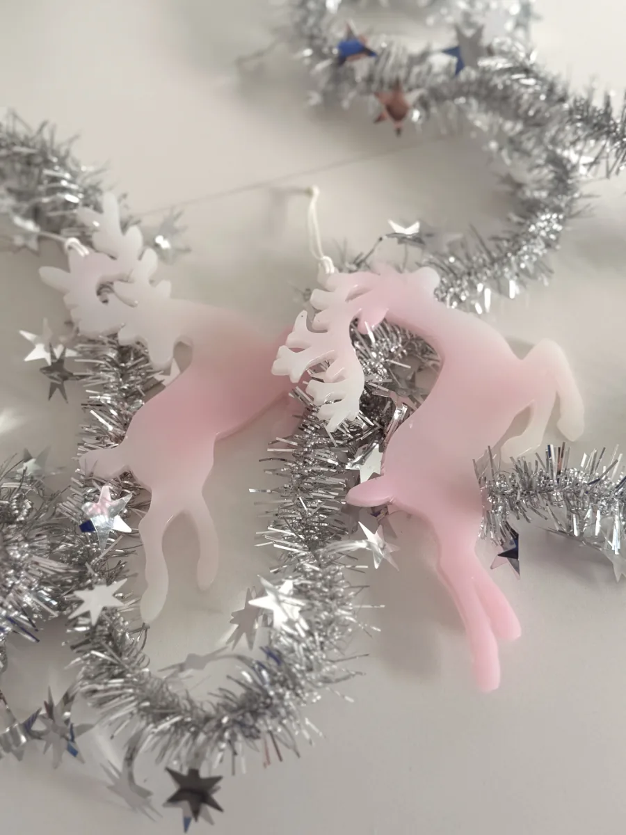 Deux cerfs de Noël rose et blanc posés sur des guirlandes argentées
