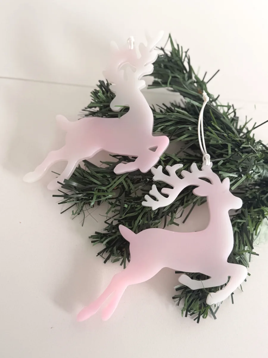 Deux cerfs de Noël en résine rose et blanc accrochés à une branche de sapin