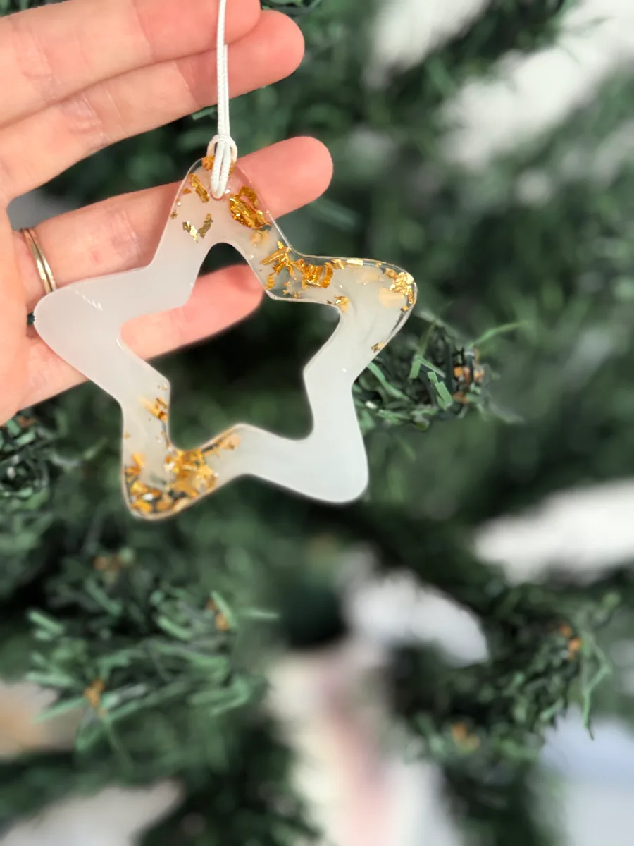 Étoile de Noël ajourée en résine blanche et dorée devant le sapin