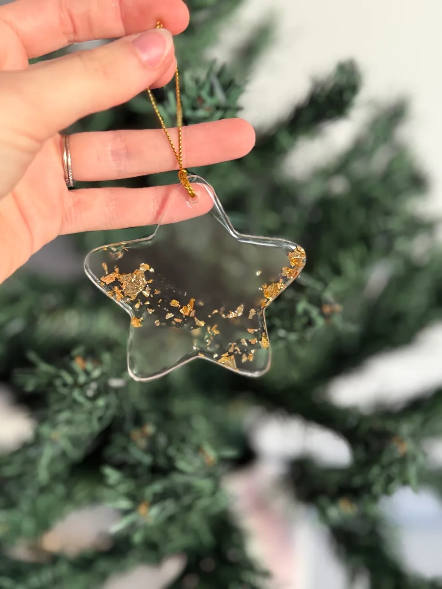 Étoile de Noël transparente pailletée d'or tenue devant le sapin