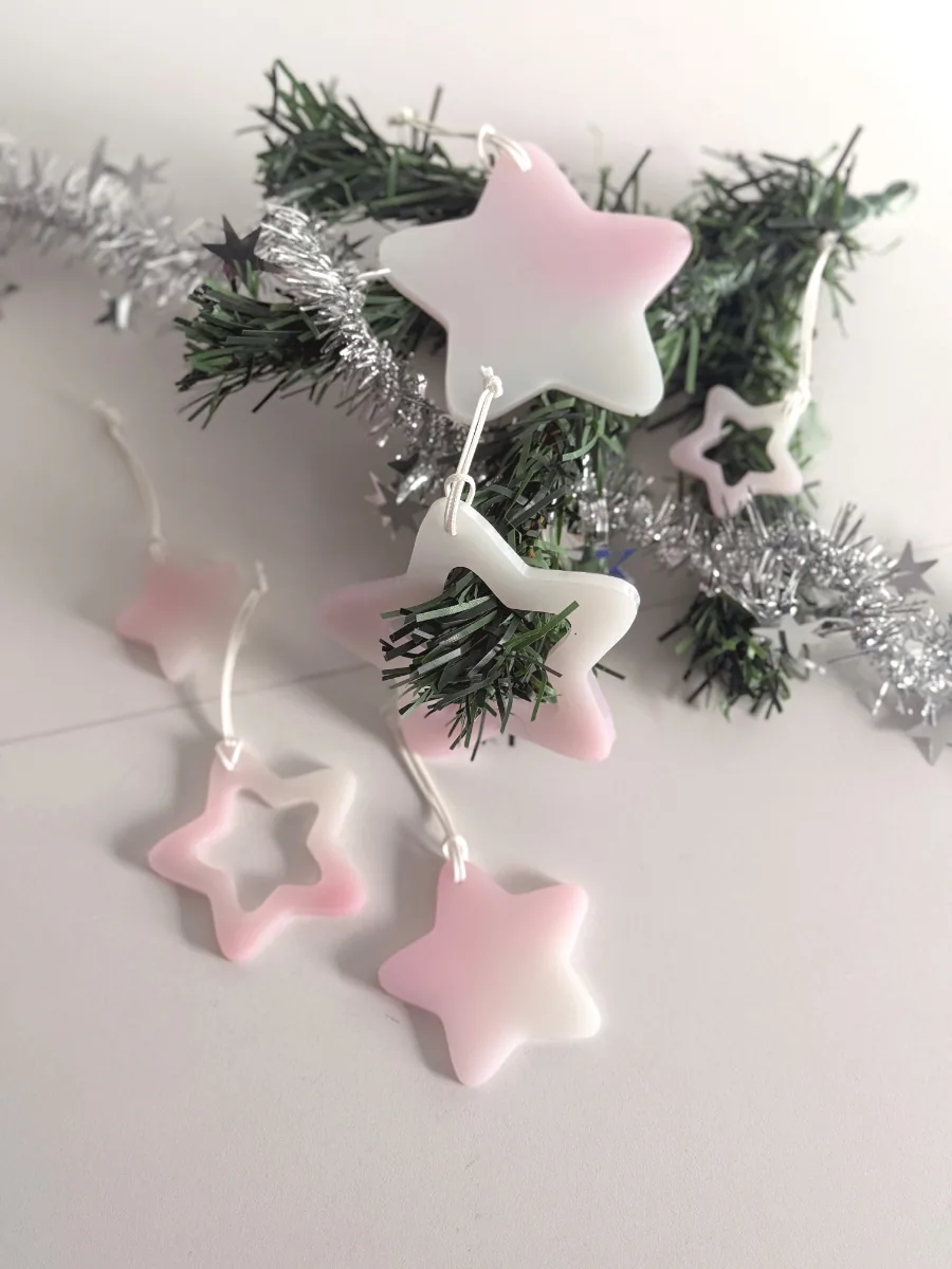 Suspensions étoile de Noël rose et blanc posées sur une branche de sapin et des guirlandes