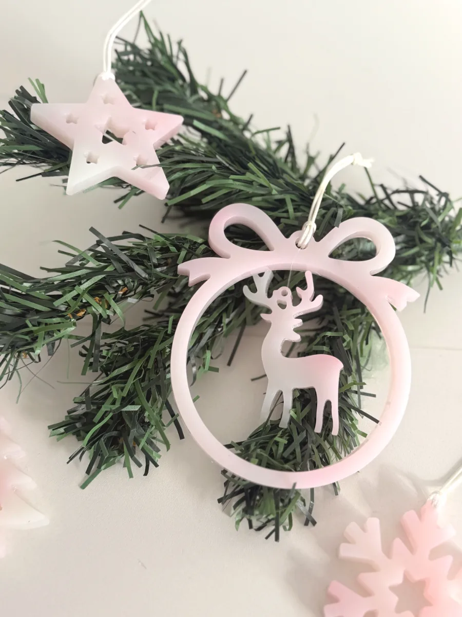 Boule à nœud rose avec cerf et étoile en résine, accrochées à une branche de sapin