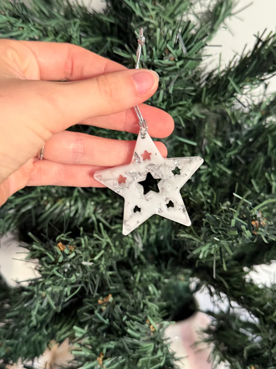 Étoile de Noël en résine blanche ajourée tenue devant le sapin